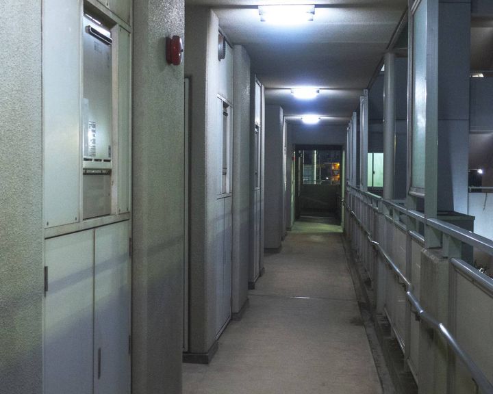 夜の集合住宅の共用廊下。玄関ドアが並び、奥まで通路が続いている。