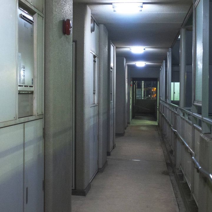 夜の集合住宅の共用廊下。玄関ドアが並び、奥まで通路が続いている。