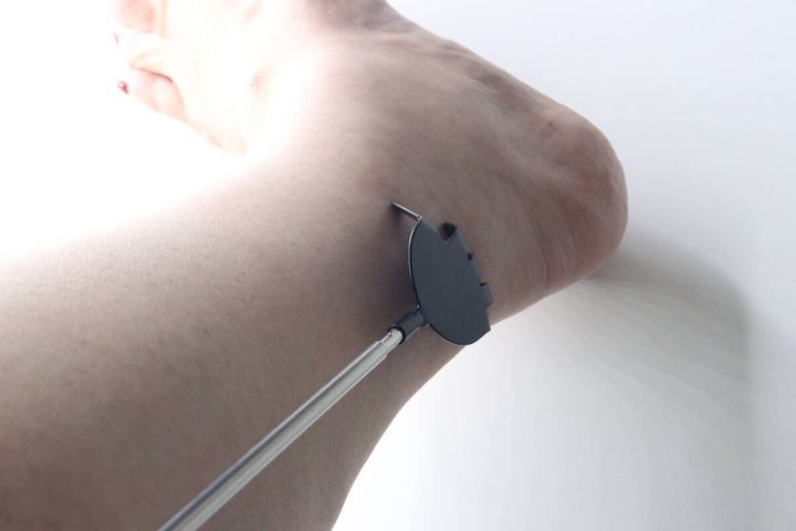 女性の足首をダイソーの孫の手の先端部分でかいている様子