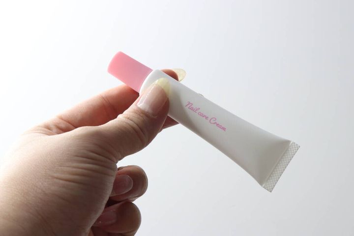 女性の手がピンクのキャップのネイルケアクリームチューブを持つ