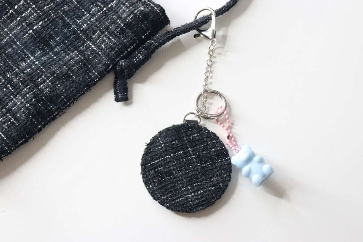 ツイード柄の巾着袋と青いクマのチャームと一緒に置かれた鏡キーホルダー
