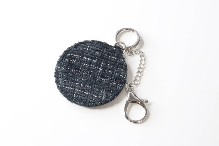 白い背景に置かれたツイード柄の黒い丸型鏡キーホルダーと金具