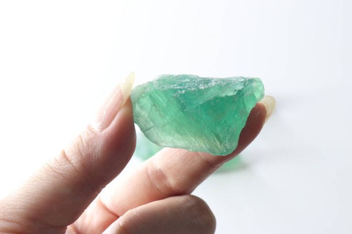 指でつまんで見せている、透明感のある緑色の天然石（グリーンフローライト）のアップ