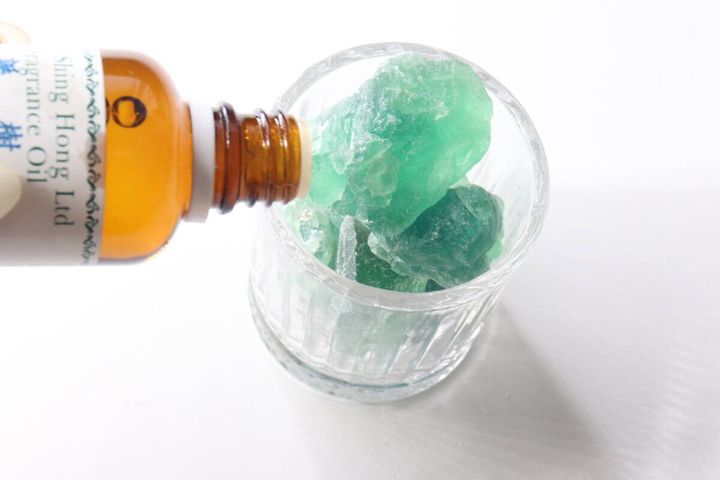 グラスに入れたグリーンフローライトの天然石に、アロマオイルの瓶からオイルを垂らしている様子