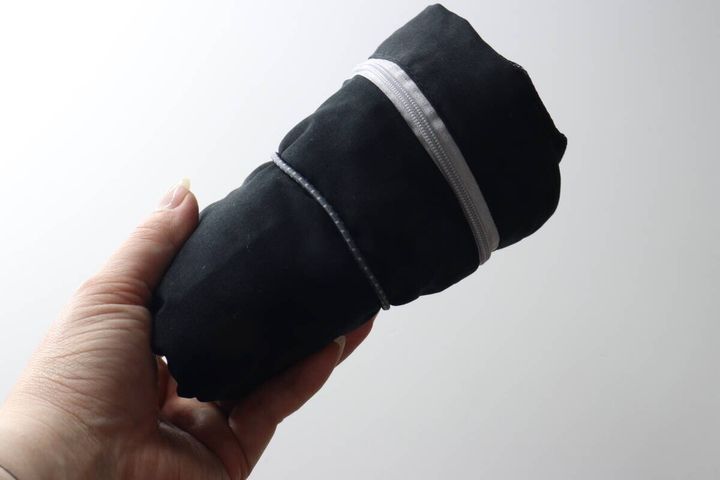 女性の手のひらに、ゴムでコンパクトにまとめられた黒い衣類圧縮バッグが乗っている。