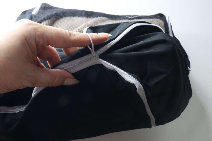 女性の指が、圧縮バッグの側面にある白いファスナーのリング状の引き手を引いて閉めようとしている。