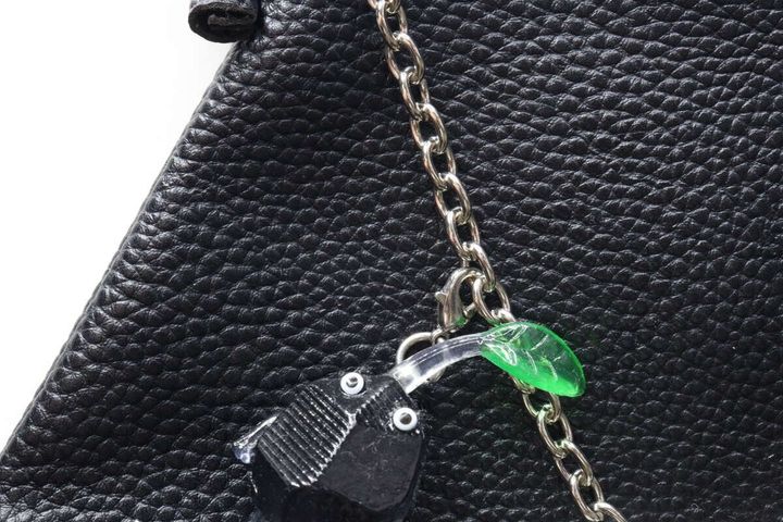 黒いバッグに取り付けられたチェーンに、緑色の葉っぱと黒いキャラクターのチャームが引っ掛けられているクローズアップ
