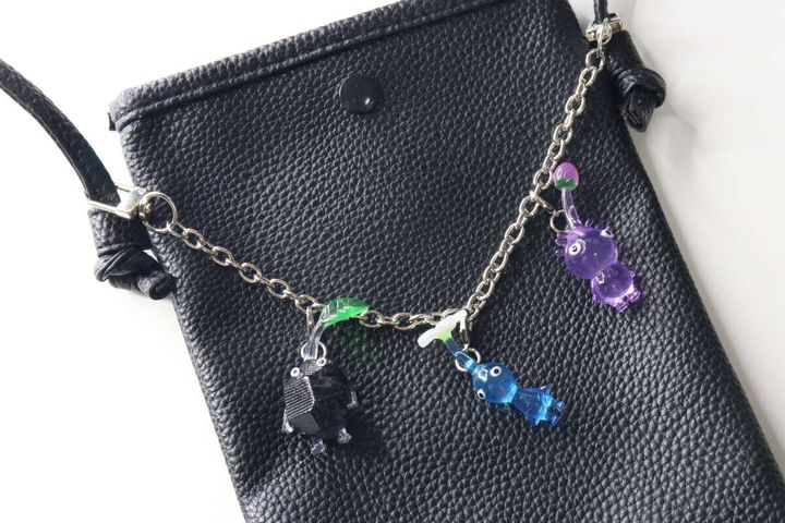 黒いショルダーバッグのチェーンに、黒、緑、青、紫の複数のキャラクターチャームがバランスよく飾られている様子