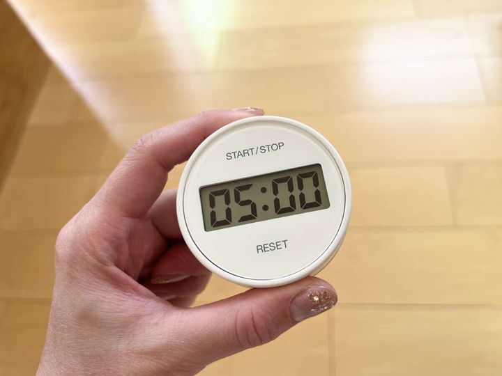 女性の手が「05:00」と表示された白いキッチンタイマーを持っている