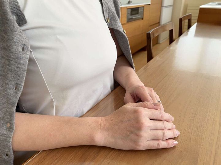 木のテーブルに腕を組んで座る女性の手元、指にはネイルが施されている