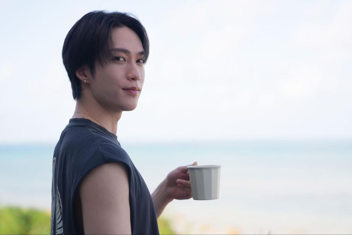 男性が、八重山の海を眺めながらフローティングブレックファストを楽しむ様子。コーヒーカップを片手にカメラを振り返るカット