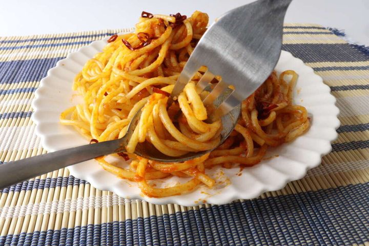 トマトソースのパスタをステンレス製スプーンとフォークで絡め取っている様子