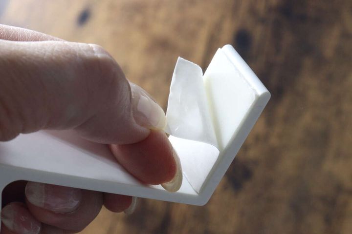 白いコーナーフックの裏面に貼られた接着テープの剥離紙を剥がしている手元