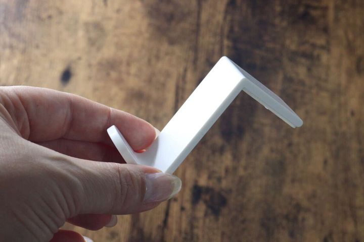 白いL字型のコーナーフックを指でつまんで持っている様子。商品の形状がよくわかる。