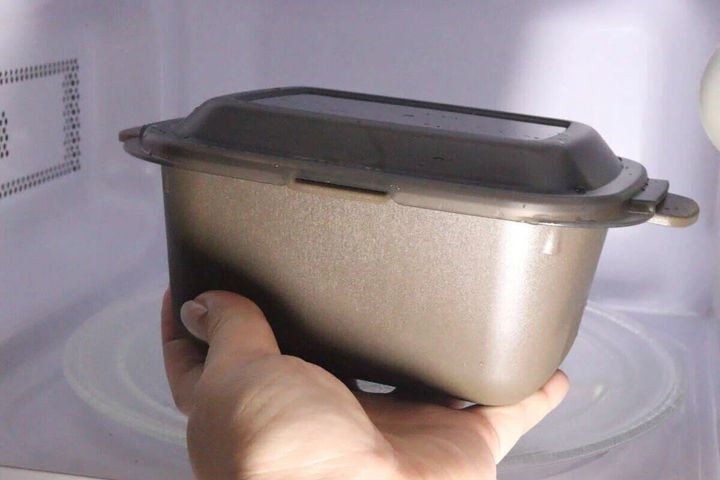 右手でレンジ調理マルチクッカーを電子レンジに入れている