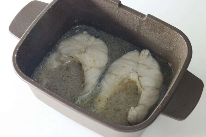レンジ調理マルチクッカーの中に煮汁に浸かった魚の切り身が2切れ