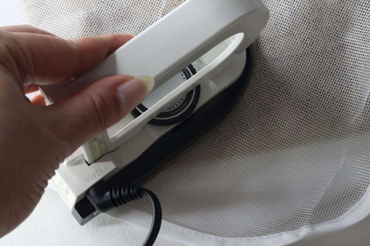 白いアイロンを使い、ワッペンを白い布に接着している手元