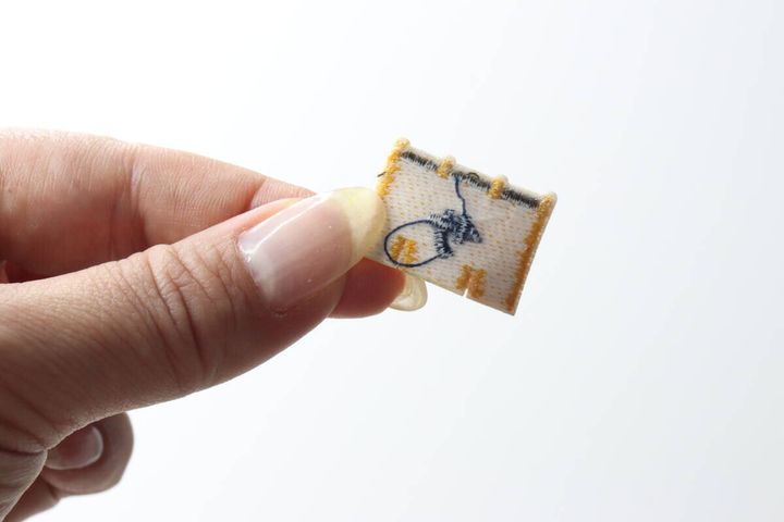剥がしたサウナモチーフのワッペンを指でつまんで見せている手元
