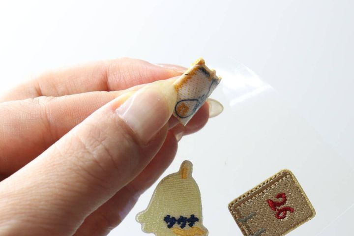 指でサウナモチーフのワッペンを透明なシートから剥がしている手元
