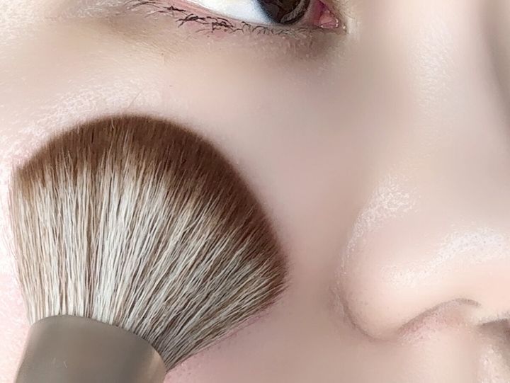女性の頬にパウダーブラシでフェイスパウダーを塗布している