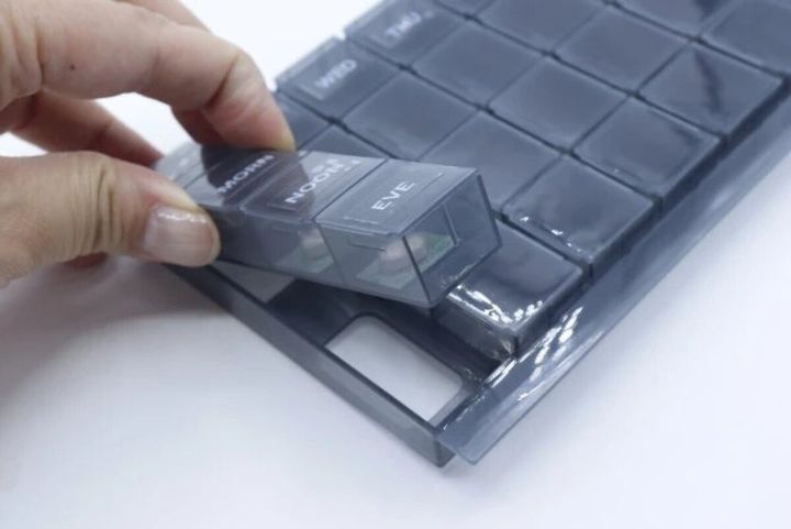 女性の指が、グレーの7DAYSピルケースから1日分のケースを取り出している