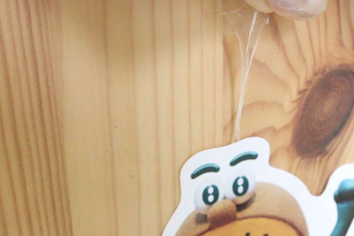 木目調の壁からキウイのキャラクターカードを剥がす際、透明なテープが長く伸びている様子