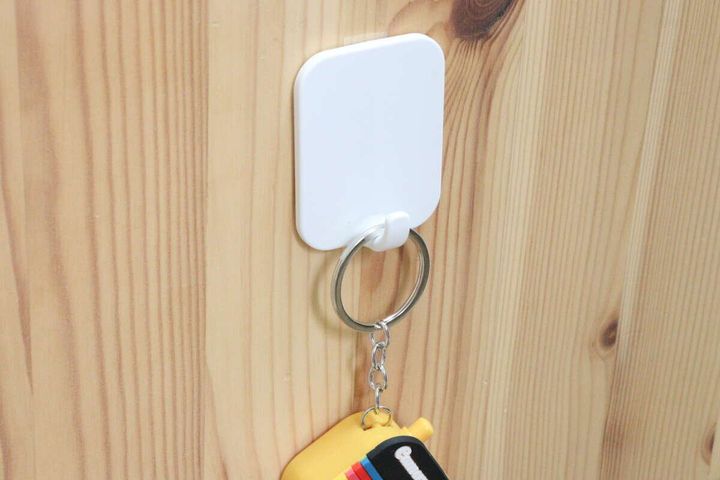 木目調の壁に透明な伸びるテープで固定された白いフックに、黄色いキーホルダー付きの鍵が吊り下げられている