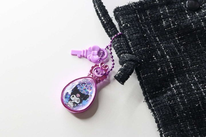 黒いツイード素材のバッグに、紫色のクロミのジュエルキーホルダーが付けられている