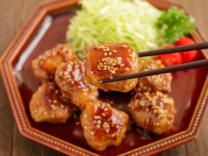 箸で持ち上げられた、白いりごまが振られた豚こまボールの照り焼き