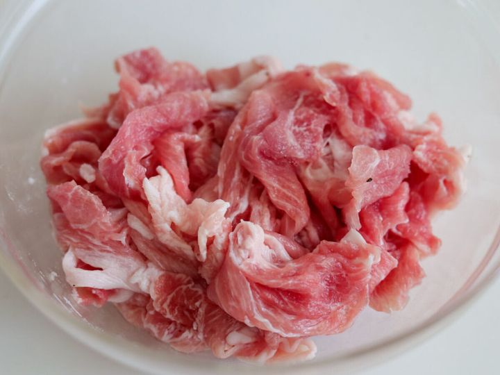透明なボウルに入った生の豚こま切れ肉のアップ