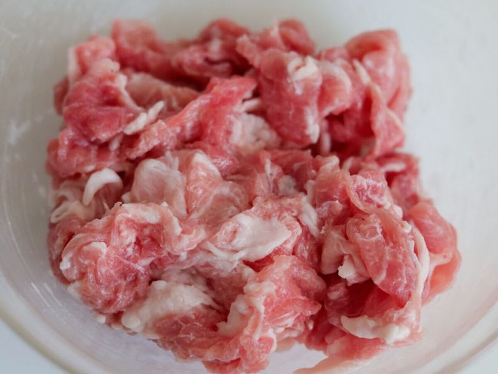 透明なボウルに入った、下味を揉み込んだ豚こま切れ肉のアップ