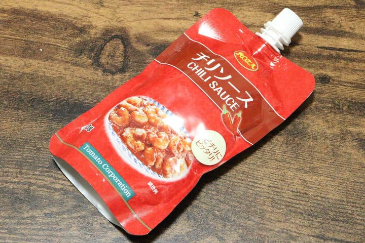 木目のテーブルに斜めに置かれた赤いパウチ容器のチリソース