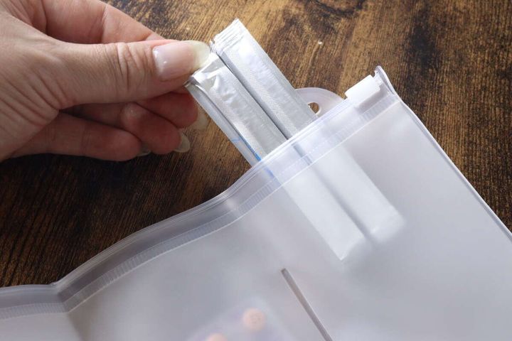 女性の手が半透明の仕切りポーチに粉薬の袋を入れようとしている様子
