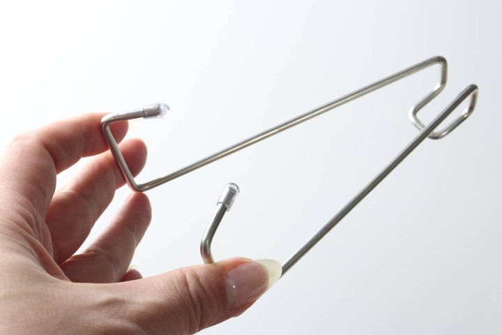 指で持った鴨居用便利フック。フックの先端には透明な保護キャップが付いている。