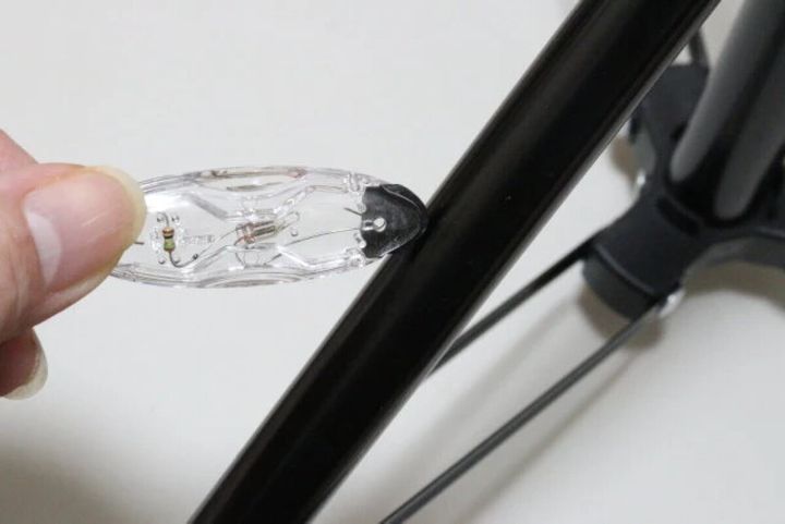 指で持った静電気除去キーホルダーを、金属製の棒に近づけている様子
