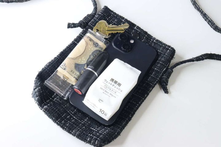 黒いツイードショルダーバッグの中にスマホ、ミニ財布、リップ、鍵、ウェットティッシュが収まっている様子