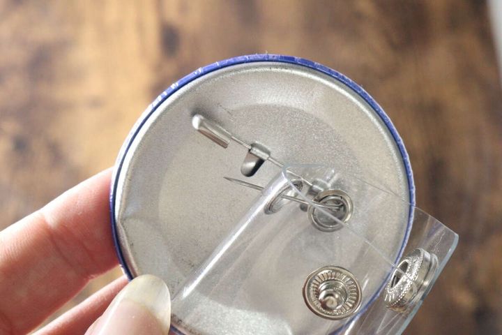 缶バッジのピンをクリアホルダーのハトメに通して装着する手元