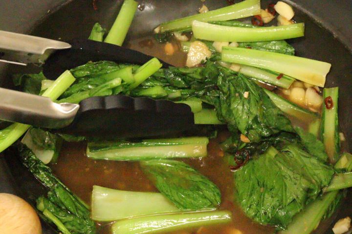フライパンの中でシリコーントングを使って青菜の野菜炒めを混ぜている