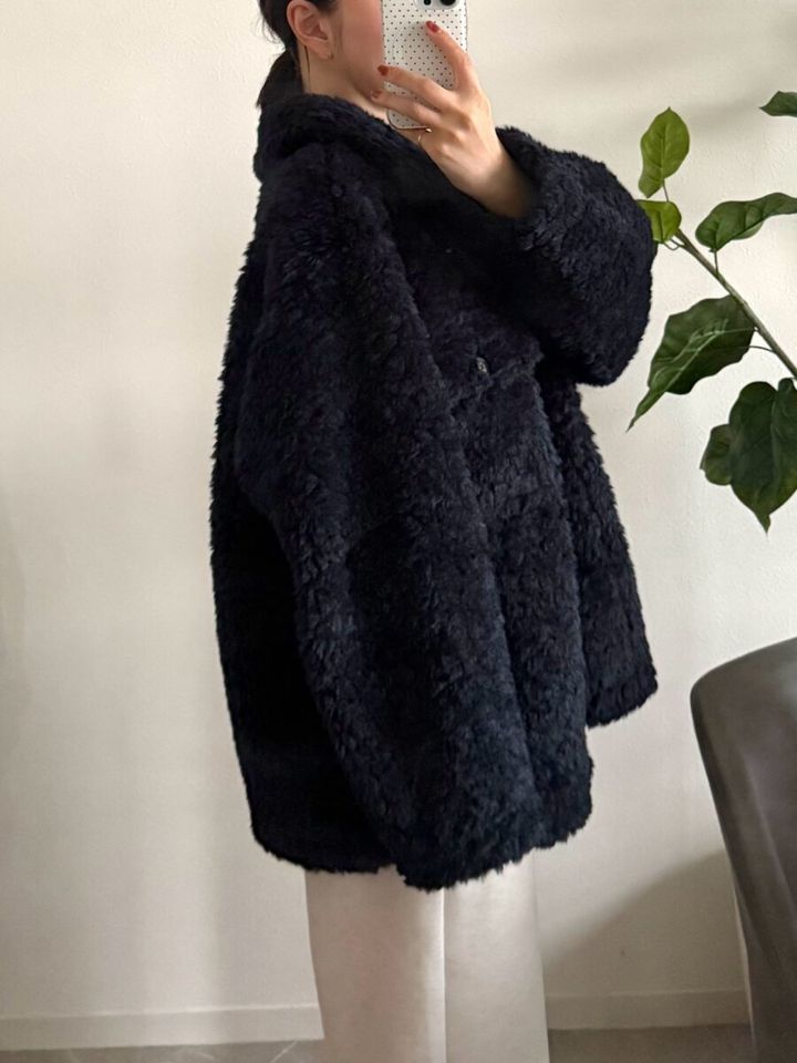 ネイビーのボアジャケットを着用した女性が、横向きでスマホで自撮りしている