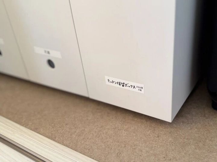 白い収納棚の扉に「キッチン保管ボックス 202X年 5月」と手書きされたラベルが貼られている