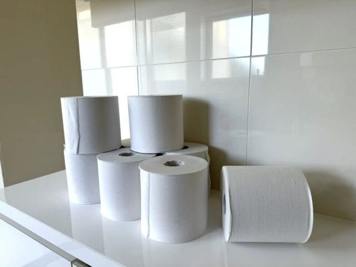 白いタイル壁を背景に、白いトイレットペーパーが複数個、棚の上に置かれている