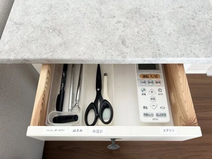引き出しの中に、ペンやハサミ、体温計、エアコンのリモコンが仕切りを使って整理されている