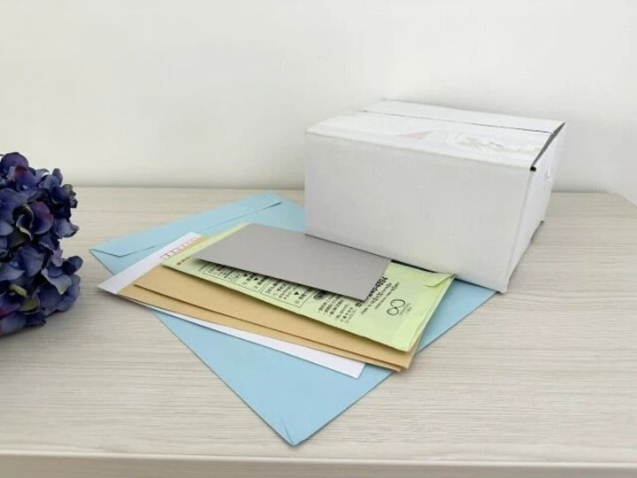 白いテーブルの上に、青や茶色の封筒、白い箱など郵便物が複数置かれている