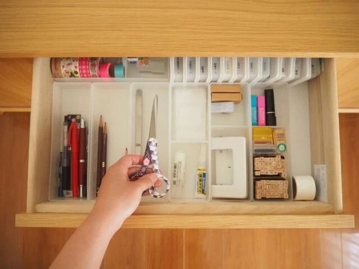 引き出しの中に文房具が仕切りで整理されており、女性の手が花柄のハサミを取ろうとしている