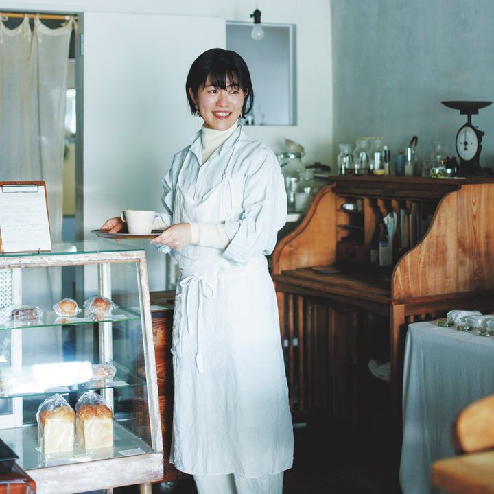 シャツにエプロンを重ね、店内でカップを持つ鈴木菜々さん