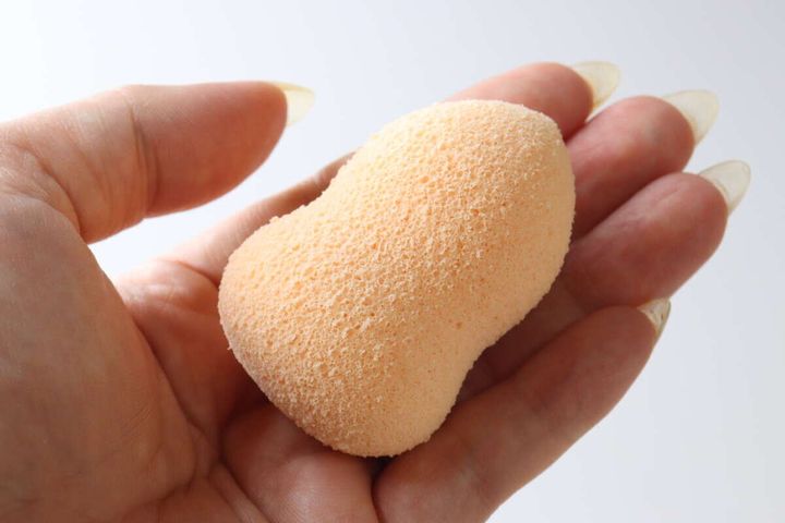 女性の手のひらに乗せられた、きめ細かいひょうたん型の洗顔パフ