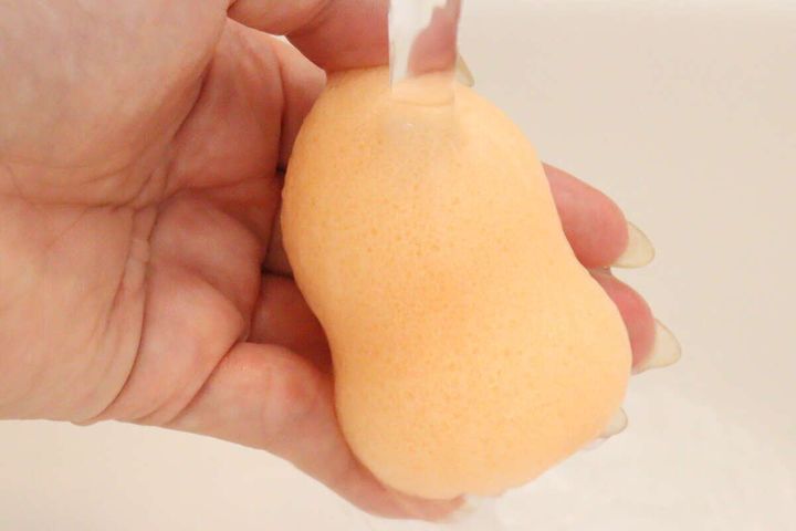 蛇口から流れる水でひょうたん型の洗顔パフを濡らしている手元