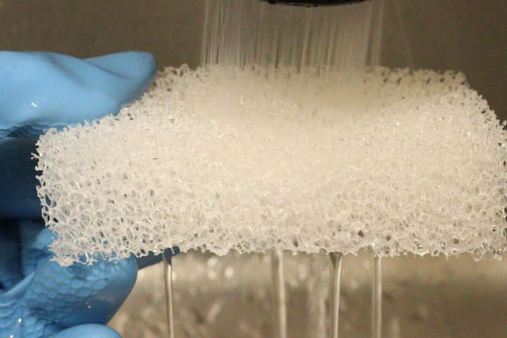 青いゴム手袋をはめた手が、水キレの良いスポンジに水を流している様子