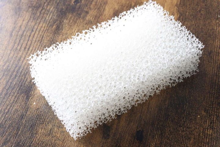 木目調のテーブルに置かれた、白い粗目のウレタンフォーム製キッチンスポンジ