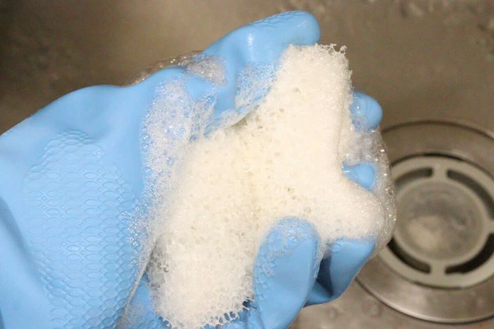 青いゴム手袋をはめた手が、スポンジを揉んで洗剤を泡立てている様子